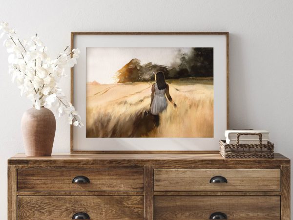 framed print of girl walking in a field at sunset