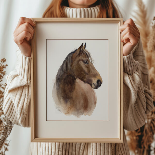 brown horse watercolour print in a light bown frame, being held by a woman in a cream jumper