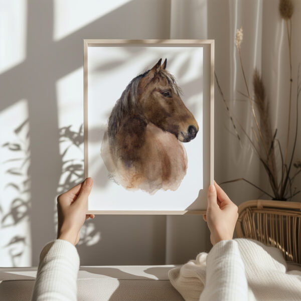 brown horse watercolour print in a light bown frame, being held by a woman in a cream jumper in neutral decor surroundings